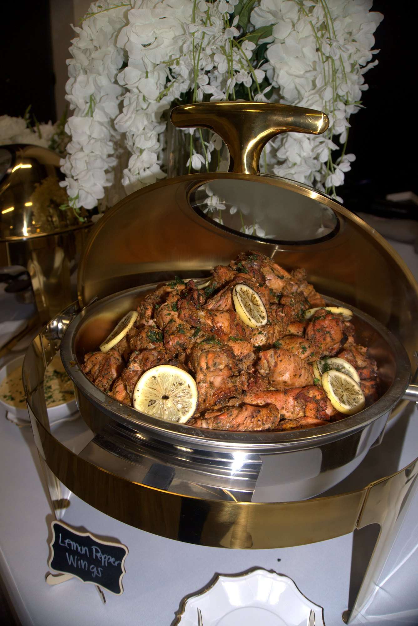 Lemon pepper wings in an open gold chafing dish beneath white florals