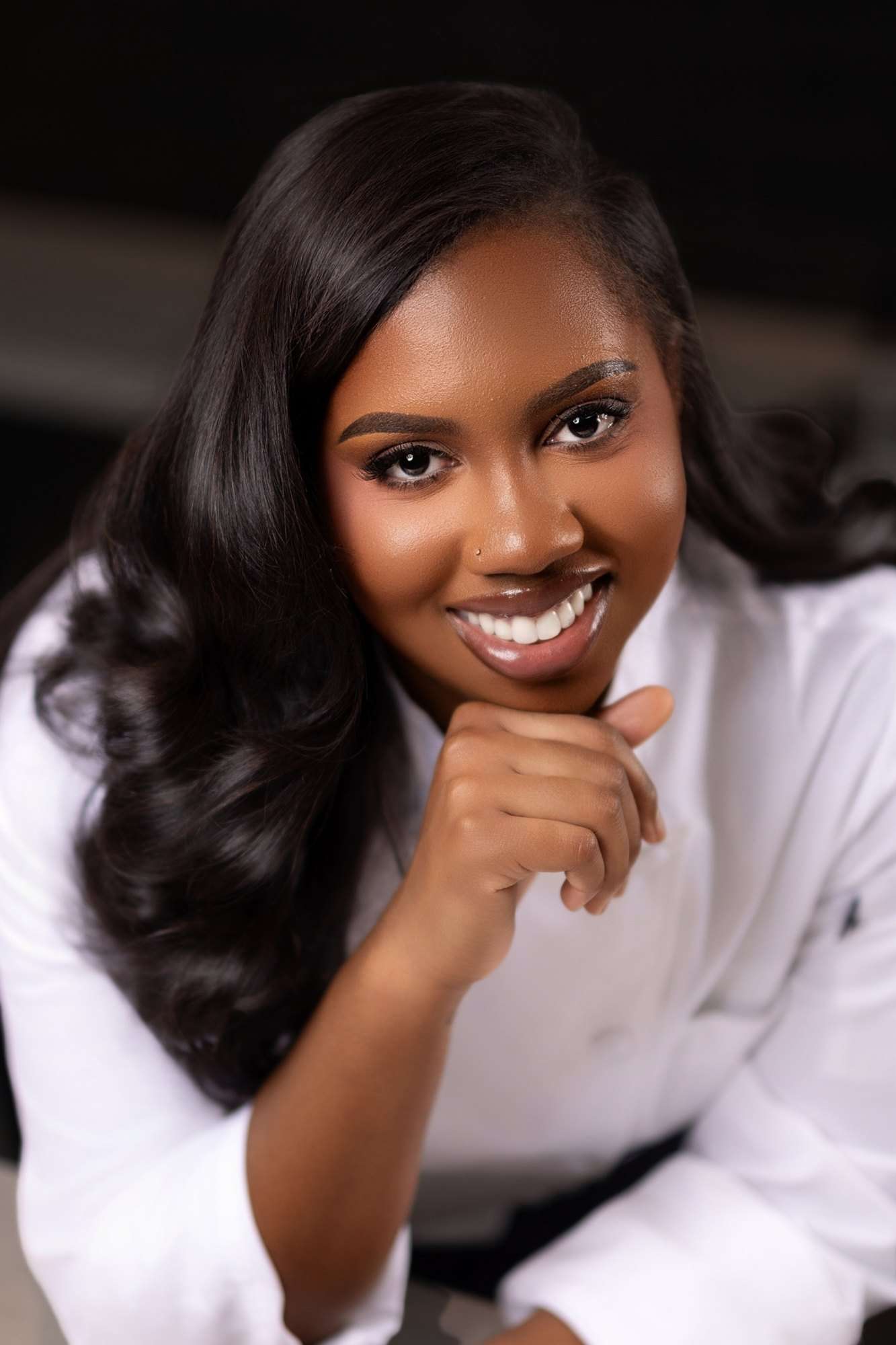 Jordan Ali-Taylor in chef whites, smiling, chin resting on one hand