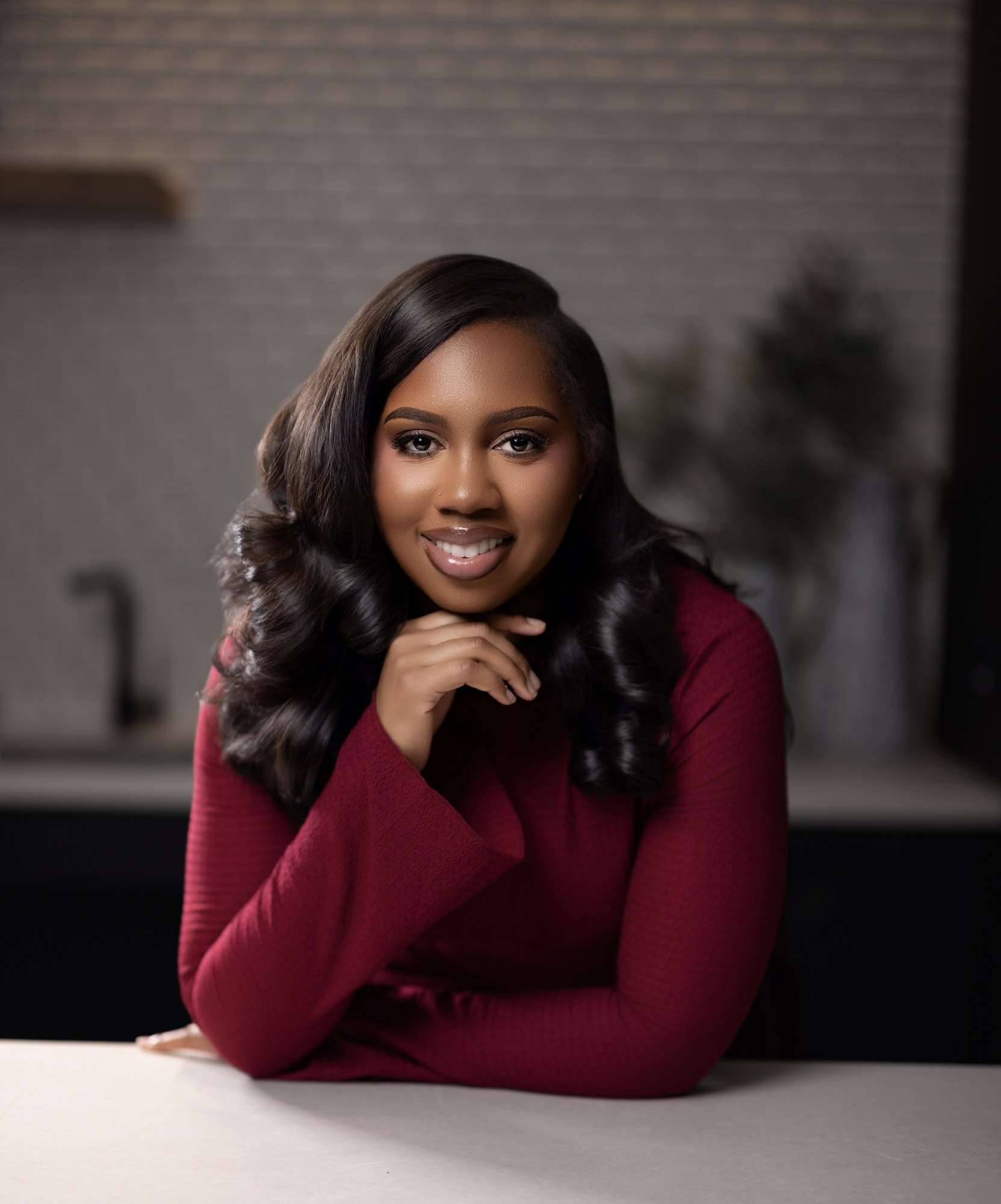 Portrait of Jordan Ali-Taylor in a burgundy knit dress, chin resting on one hand