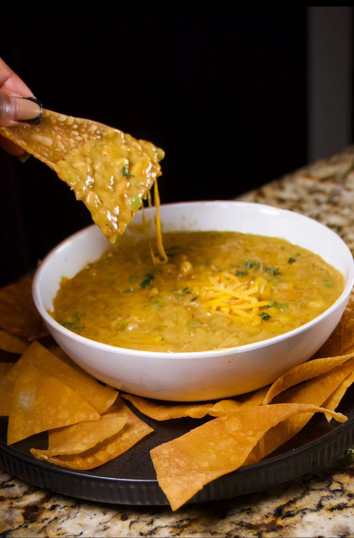 A tortilla chip pulled from a bowl of cheese dip, cheese stretching