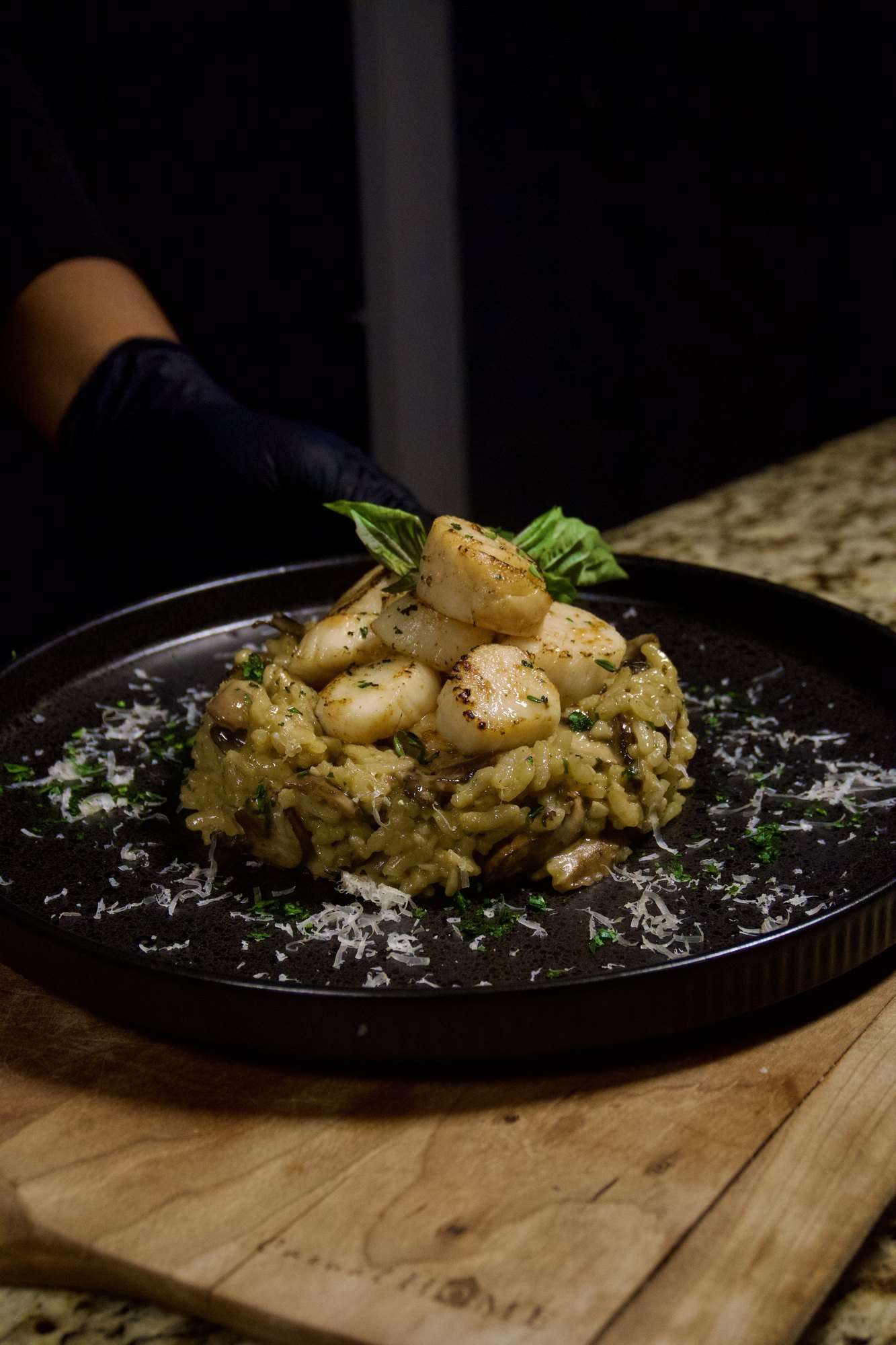 Seared scallops on mushroom risotto with grated cheese and basil on a dark plate