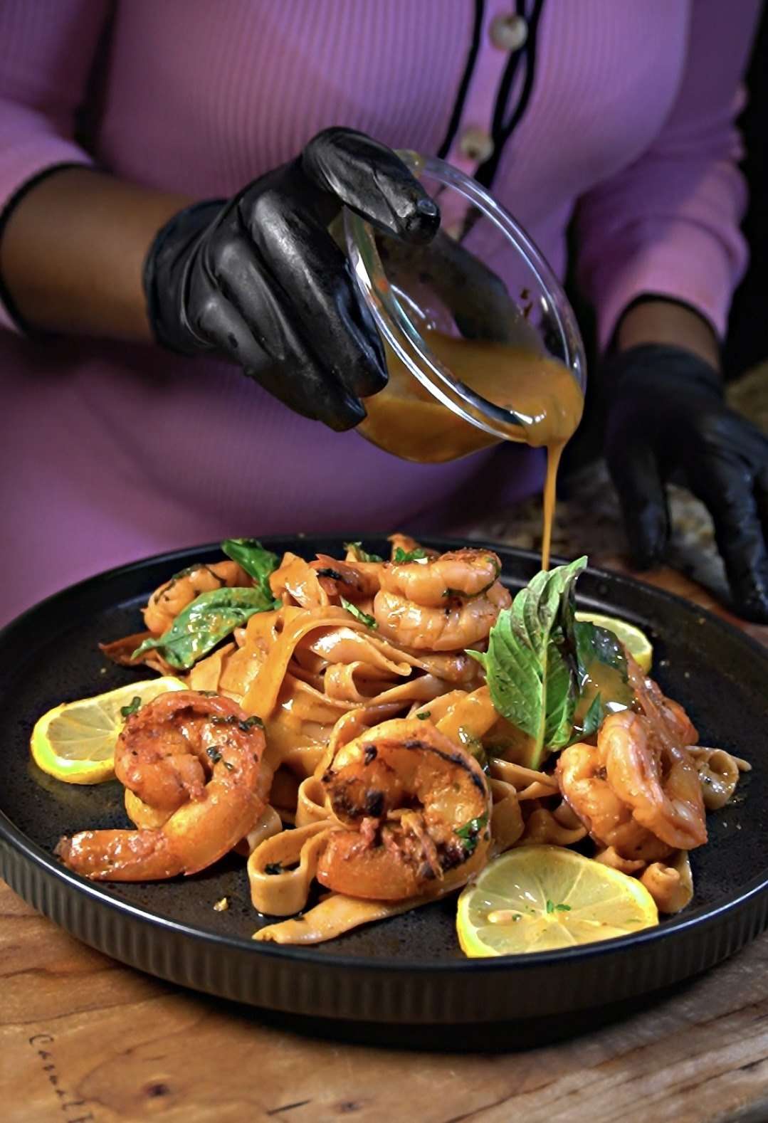 Sauce being poured over grilled shrimp and pasta with lemon and basil