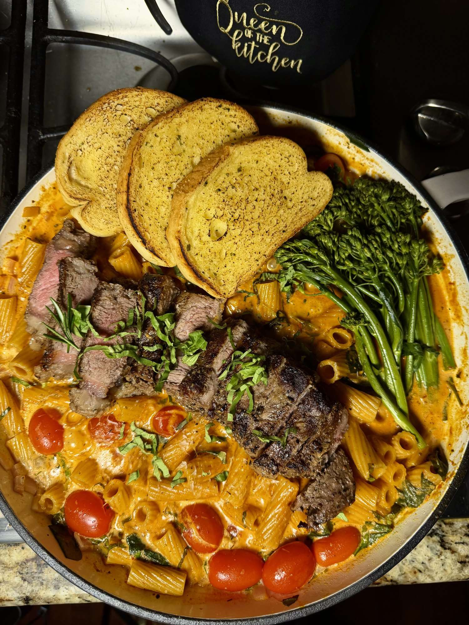 Sliced steak on creamy rigatoni with broccolini, roasted tomatoes and garlic toast